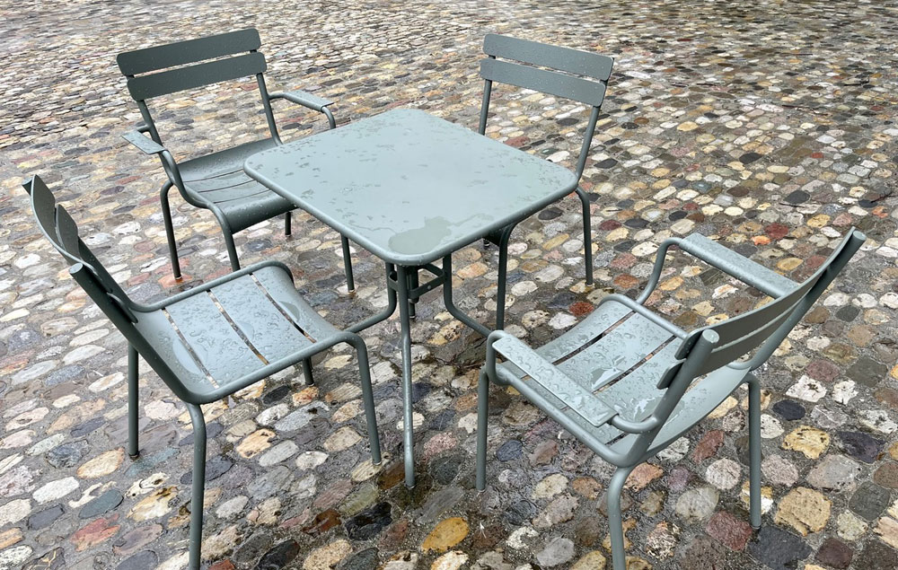 Fermob «Luxembourg» Gartenmöbel in der Farbe «Rosmarin» im Regen auf Kopfsteinpflaster