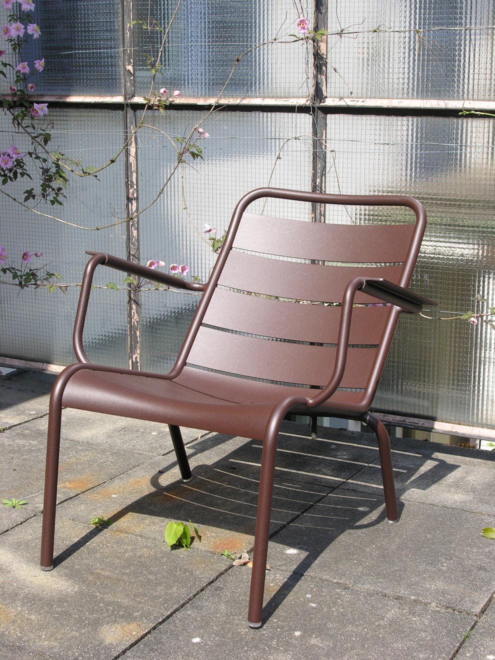 Tiefer Luxembourg Sessel von Fermob in der Farbe Rost vor einer Glaswand