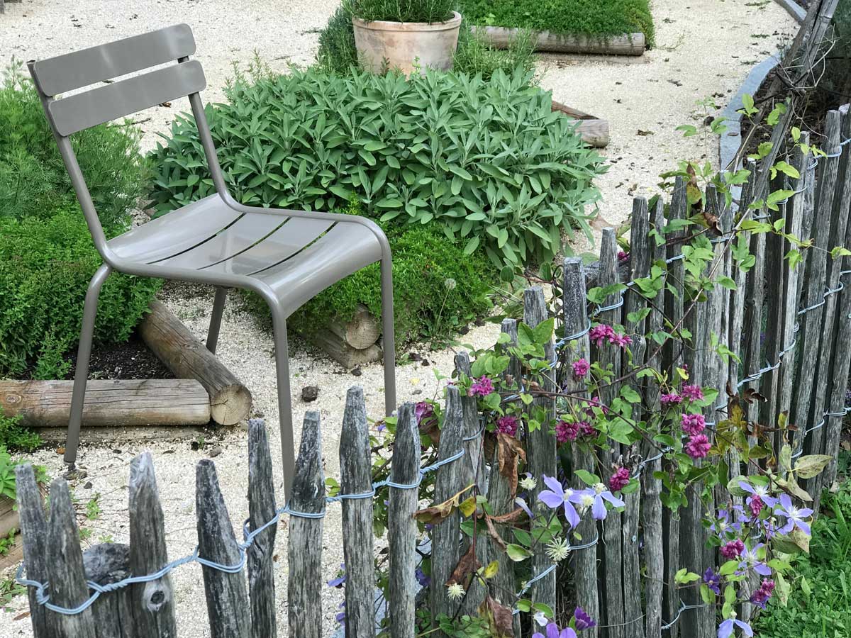 Luxembourg Gartenstuhl in der Farbe «Schlamm» in einem Garten mit Kräutern und Clematis
